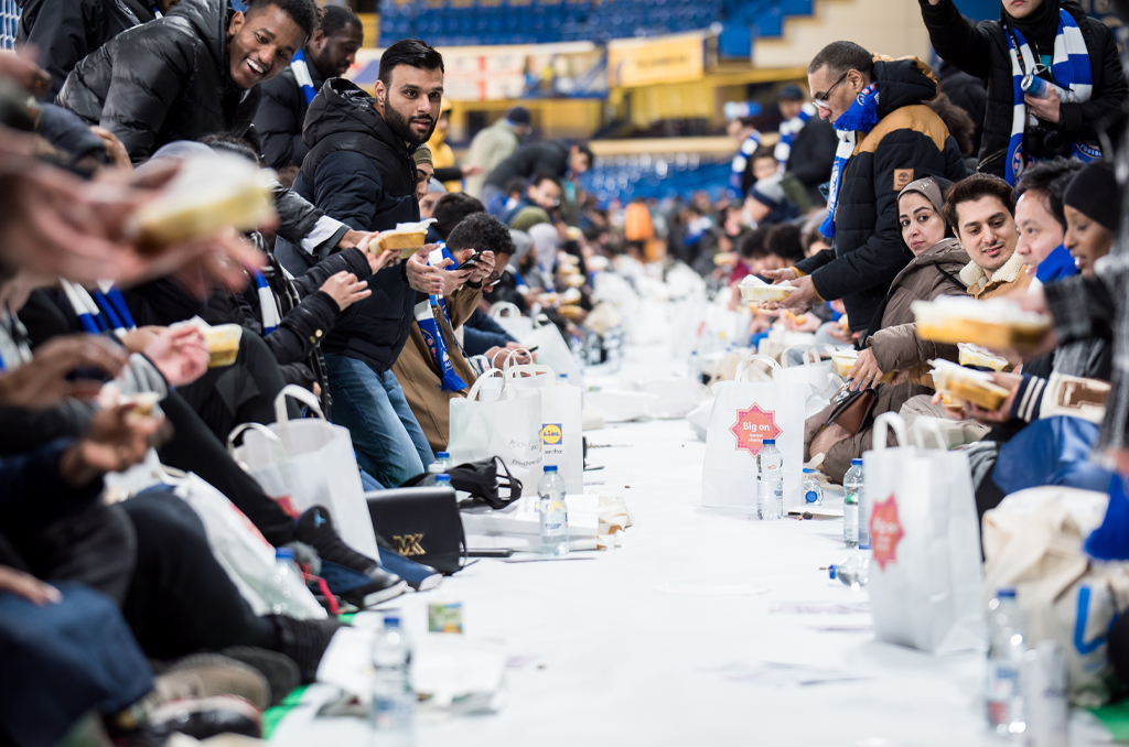 A lot of people sitting on the chairs, enjoying their lunch with many water bottles and shopping bag laying on the table.