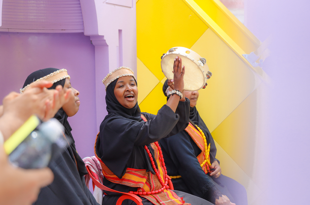 Three ladies wearing black burka in which on of them is singing some with musical instrument .