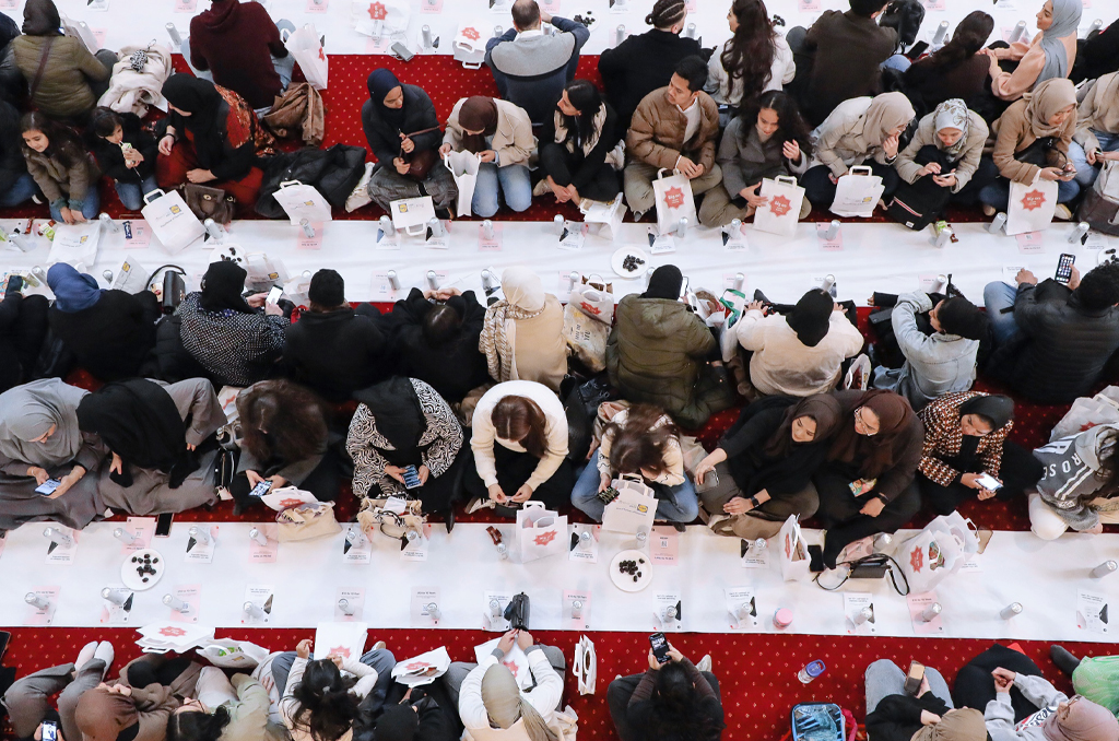 A lot of people sitting on the red carpet to open their fast with a bunch of dates and water.