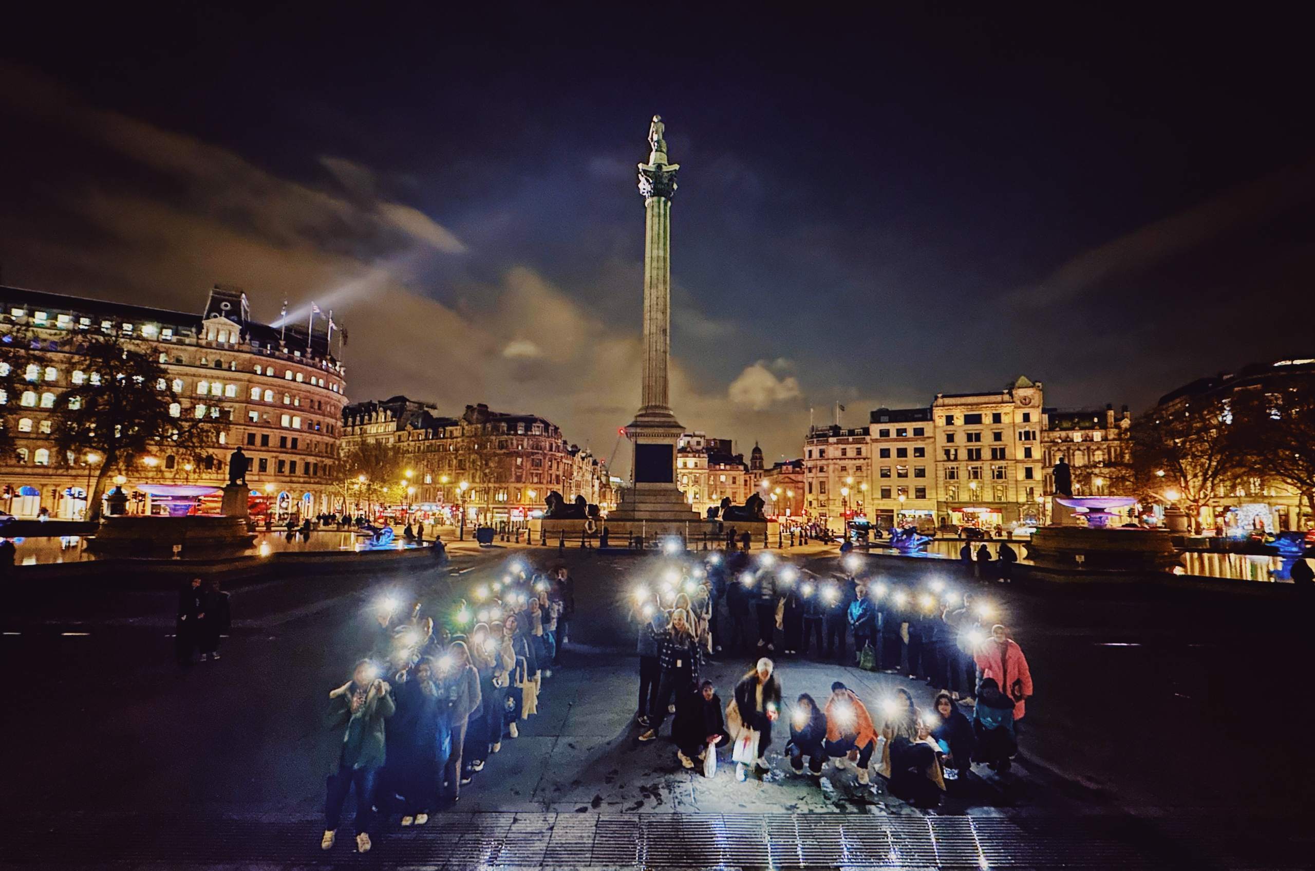 A lot of people showing the flashlights of their phone with the beautiful buildings on the back.