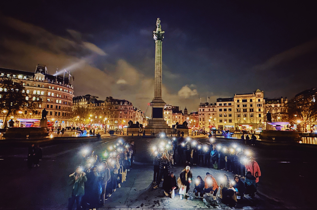 A lot of people showing the flashlights of their phone with the beautiful buildings on the back.