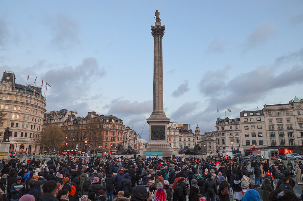 A lot of people standing with a tall and huge buildings on the back somewhere in the world.